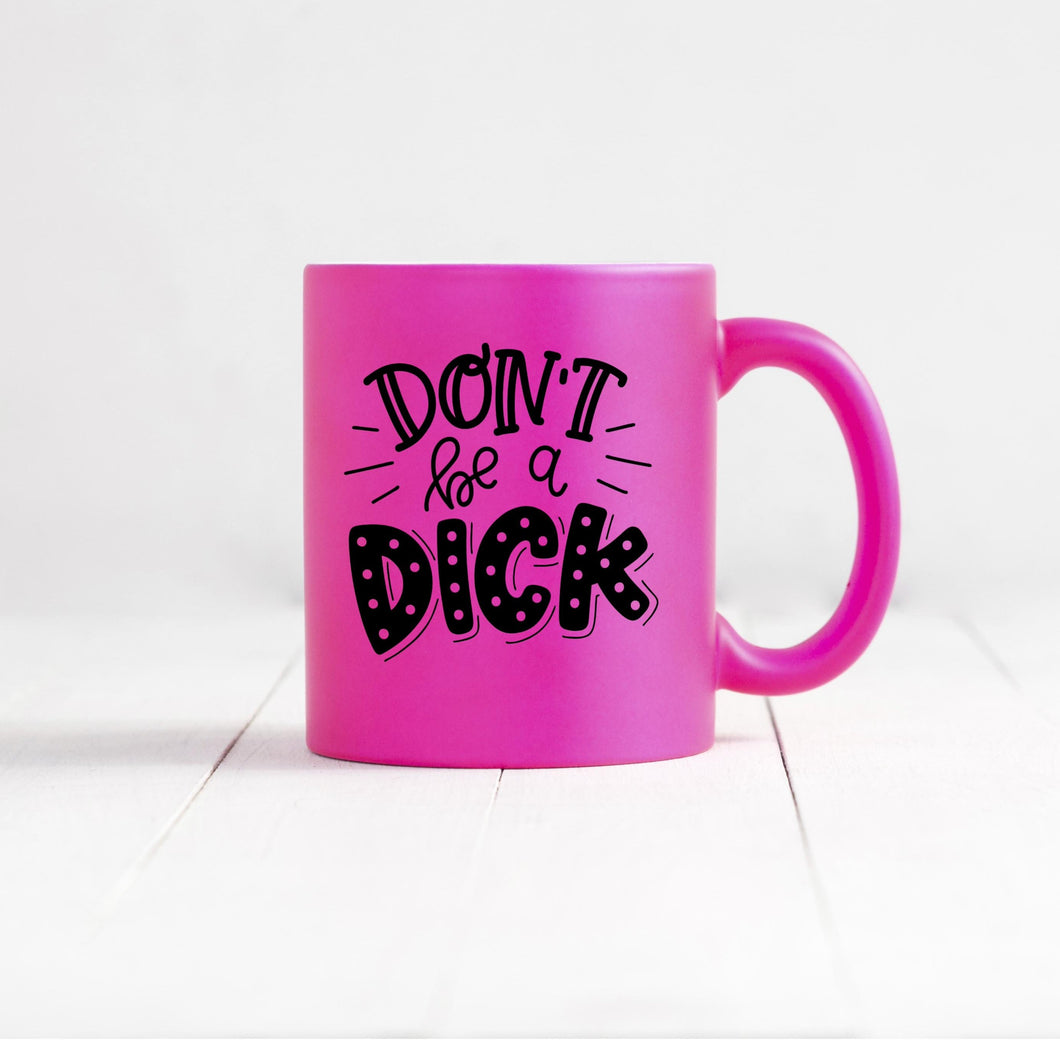 don't be a dick hot pink coffee mug sitting on wood
